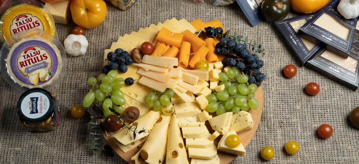 Aesthetic cheese platter with fresh grapes and vegetables on burlap background, ready for serving.