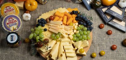 Aesthetic cheese platter with fresh grapes and vegetables on burlap background, ready for serving.