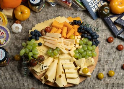 Aesthetic cheese platter with fresh grapes and vegetables on burlap background, ready for serving.