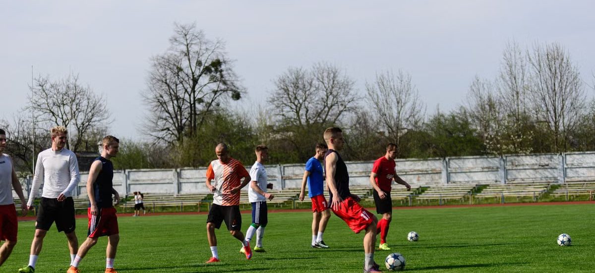 Athletes practicing soccer outdoors on a lush green field under clear skies.
