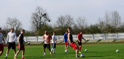 Athletes practicing soccer outdoors on a lush green field under clear skies.