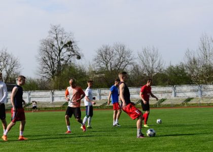 Athletes practicing soccer outdoors on a lush green field under clear skies.