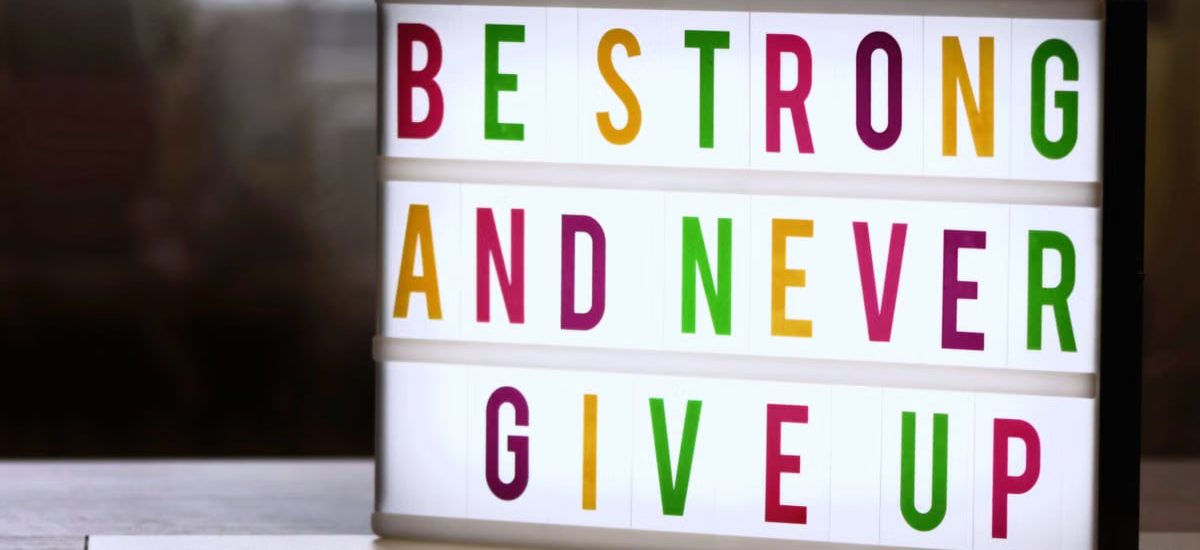 Motivational lightbox sign displaying 'Be Strong and Never Give Up.'